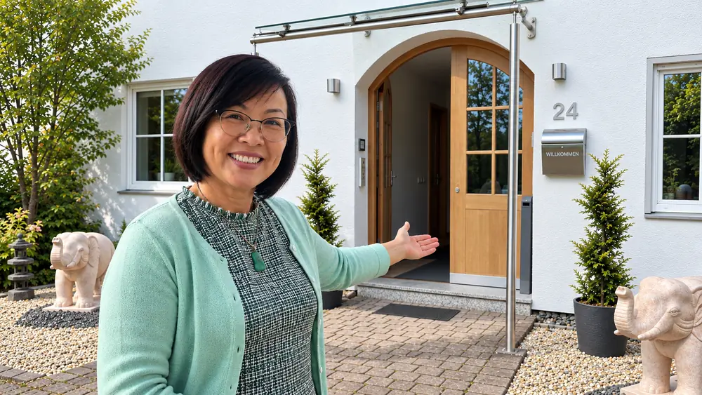 Theresa Poll zeigt einladend auf die offene Haustür der Casa Theresa